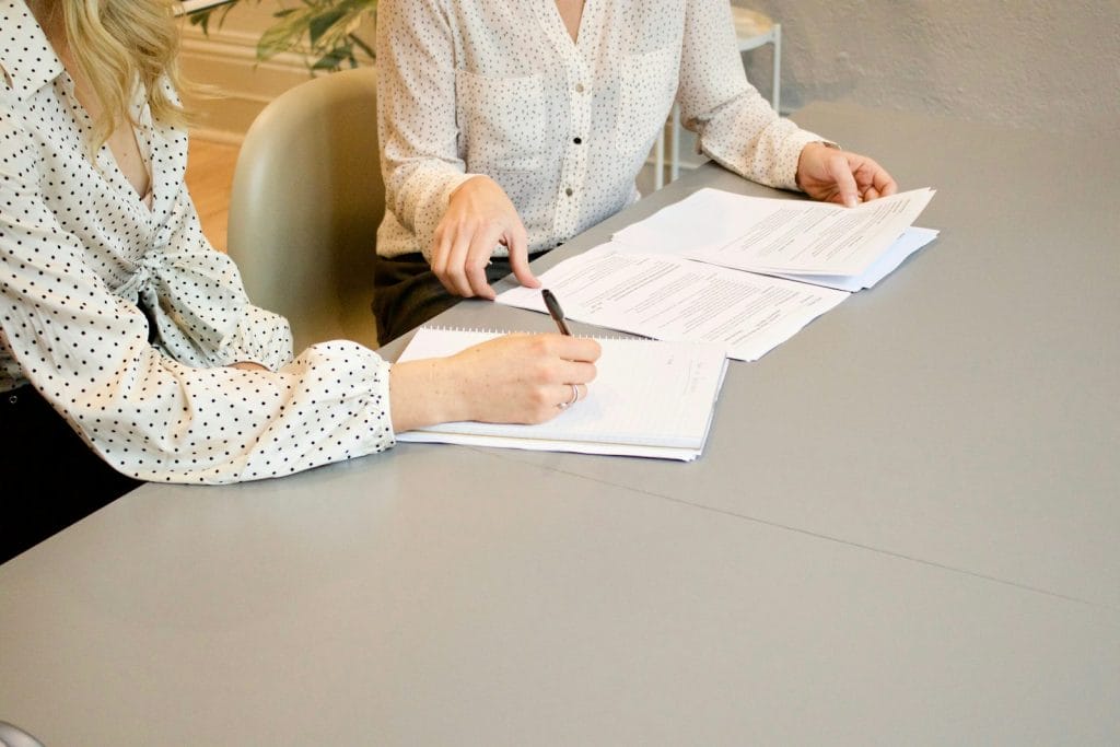 Modelo de Recurso para contestação de penalidade por infração ambiental 1 | Juristas woman signing on white printer paper beside woman about to touch the documents